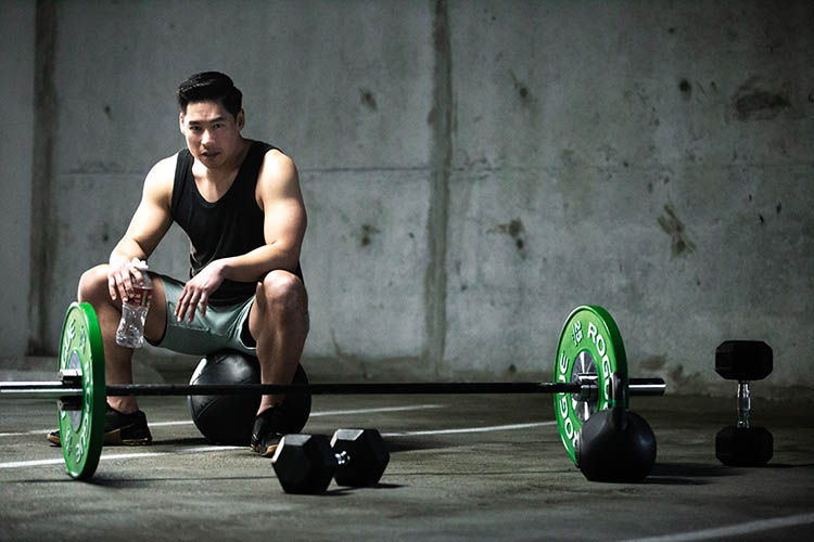 A photo of Aaron sitting on a medicine ball behind a barbell.